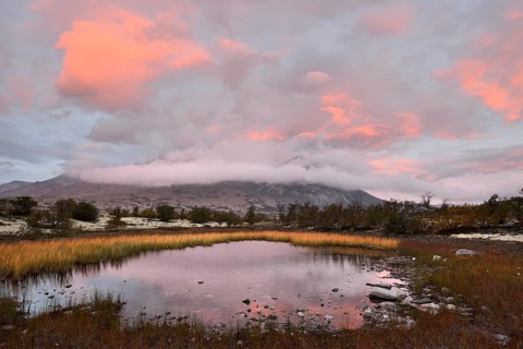 Red sky and mist in the morning above the peaks of the Stygghoin or Stygghoin mountain group reflected in a small lake