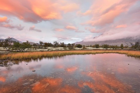 Red sky and mist in the morning above the peaks of the Stygghoin or Stygghoin mountain group reflected in a small lake
