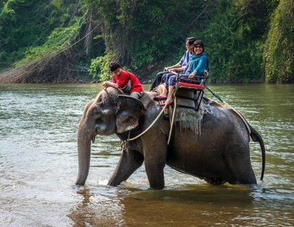 Two tourists riding elephant in water with mahout