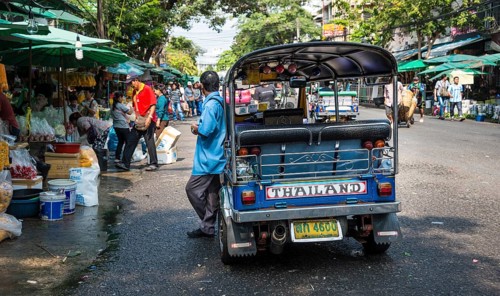 Tuk-tuk driver waiting by his car on busy road