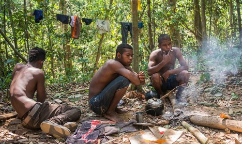 Three young aboriginal Orang Asil men sitting on the ground in the jungle