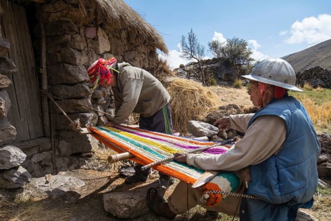 Old Indio man with helmet weaving a colorful rug with a simple loom