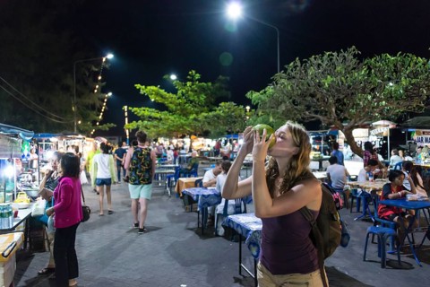 Female tourist drinking from a coconut at a night market