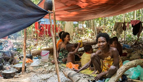 Women and children of the Orang Asil tribe sitting under tarpaulins in the jungle