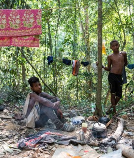Two young men of the Orang Asil tribe sitting on the ground in the jungle and making tea