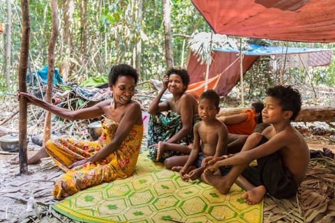 Women and children of the Orang Asil tribe sitting under tarpaulins in the jungle