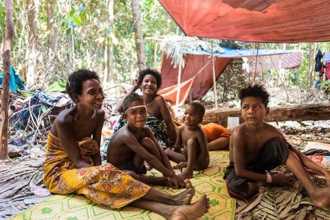 Women and children of the Orang Asil tribe sitting under tarpaulins in the jungle