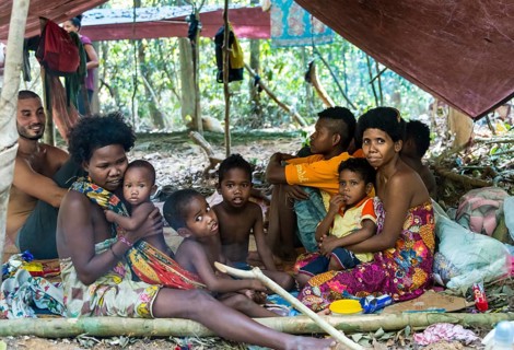 Men women and children of the Orang Asil tribe sitting under tarpaulins in the jungle