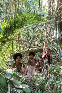 Woman of the Orang Asil tribe sitting with children under palm fronds in the jungle