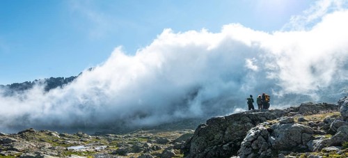 Silhouette of three hikers in front of clouds