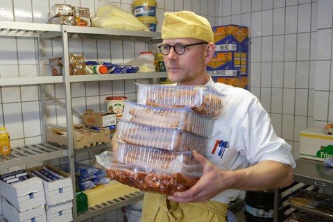Cook with meat packs in the refrigerator of a canteen kitchen