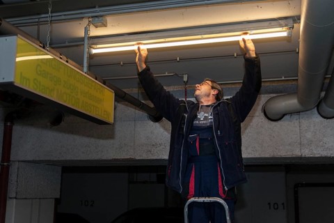 Caretaker replacing fluorescent lamp in underground garage