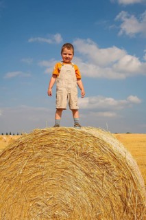 Little boy standing proudly on a straw bale