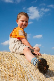 Little boy sitting on a straw bale under a cloudy blue sky