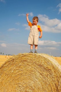 Little boy standing proudly on a straw bale