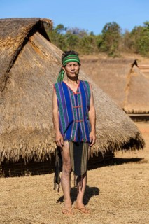 Man in traditional costume in front of a Phnong house