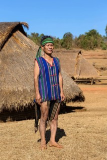 Man in traditional costume in front of a Phnong house