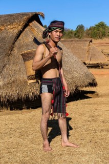Man in traditional costume in front of a Phnong house