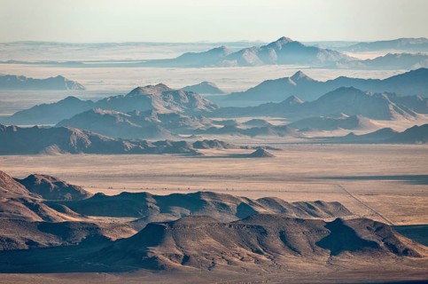 Isolated mountain ridges at edge of Namib Desert with coastal fog behind