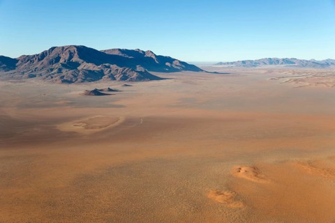 Arid desert plains with so-called Fairy Circles and isolated mountain ridges at the edge of the Namib Desert