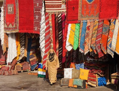 Woman in front of a shop with colourful carpets in the souks of Marrakesh