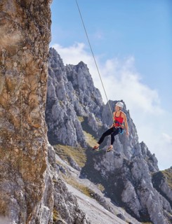 Climber with helmet swinging on climbing rope on rock face