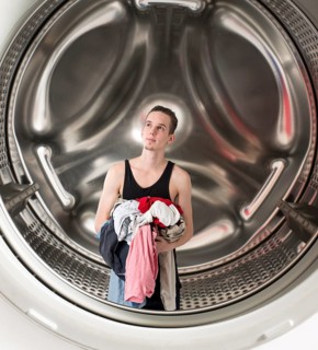 Conceptual image of a young confused man holding laundry inside a washing machine