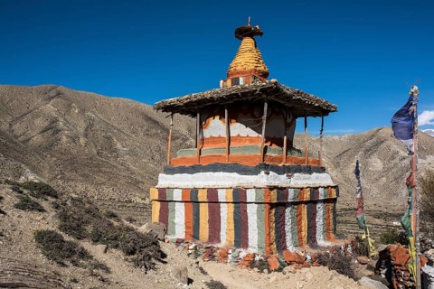 Colourfully painted Buddhist stupa in front of mountain landscape