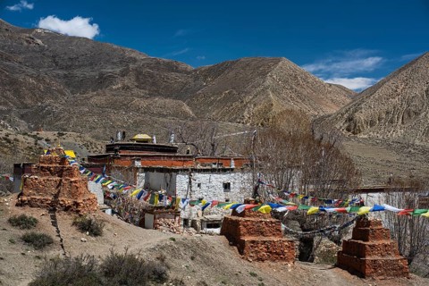 Ghar Gompa of Lo Gekar with prayer flags in front of mountain landscape