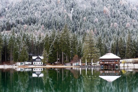 Snow-covered forest and houses reflected in Lake Toblach