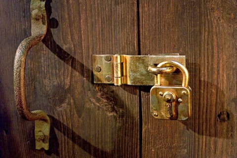 Old wooden door locked with metal fittings and a padlock