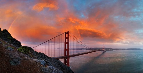 Panoramic view of the Golden Gate Bridge with a rainbow at sunset and orange-glowing storm clouds
