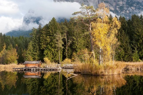 Hut and trees in autumn reflected in the Volser Weiher lake