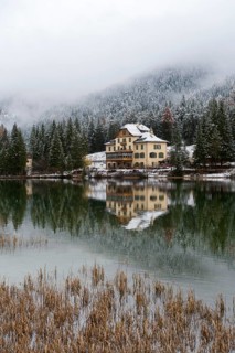 Snow-covered forest and houses reflected in Lake Toblach