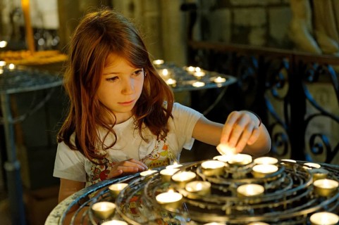 Girl lighting a devotional candle at Notre-Dame de Paris or Notre-Dame Cathedral