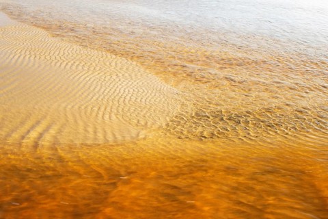 Reddish ferruginous water flows over a sandy beach at low tide