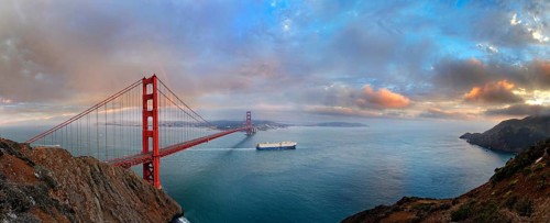 Panoramic view of the Golden Gate Bridge at sunset with a rainbow and storm clouds