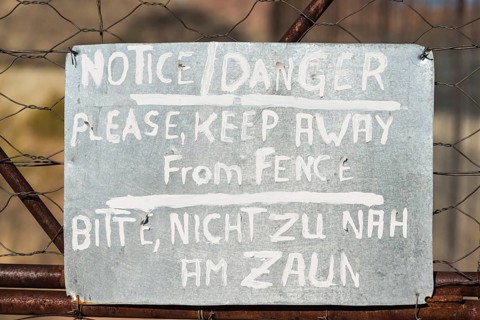 Warning sign in English and German on the fence of a predator enclosure
