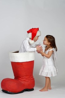 Boy in a Christmas boot handing a small Christmas present to a girl dressed as an angel