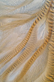 Creek with reddish ferruginous water flows over a sandy beach into the sea