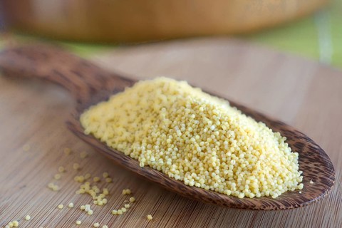 Millet grains on a wooden scoop made of coconut wood
