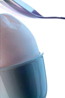 Spoon is breaking the shell of an egg in an egg cup