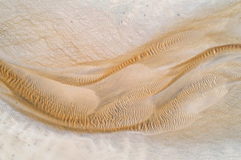 Creek with reddish ferruginous water flows over a sandy beach into the sea
