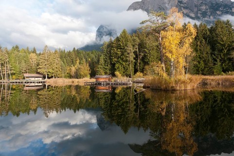 Hut and trees in autumn reflected in the Volser Weiher lake
