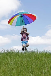 Boy with colorful umbrella jumping on meadow