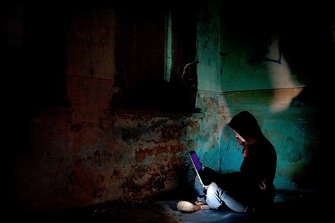 Female computer hacker sitting with a laptop in the dark