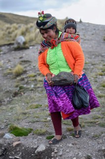 Young woman with child in a sling carrying a heavy stone to secure the shores of an artificial lake for irrigation