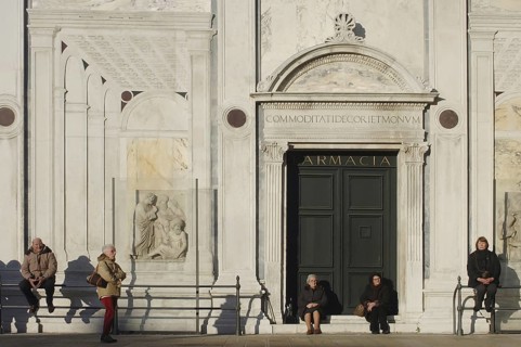 People sitting in the sun in front of a public building with a historic facade