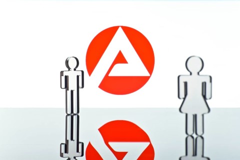 Two figures standing in front of the logo of the German employment agency