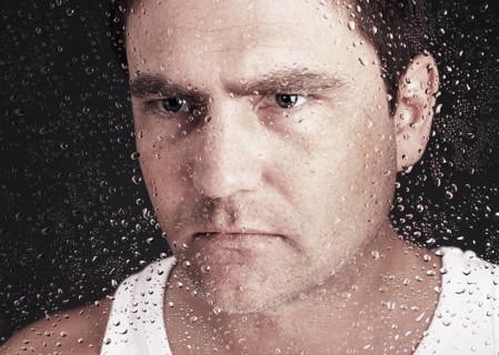 Closeup of pensive man looking through window covered with raindrops